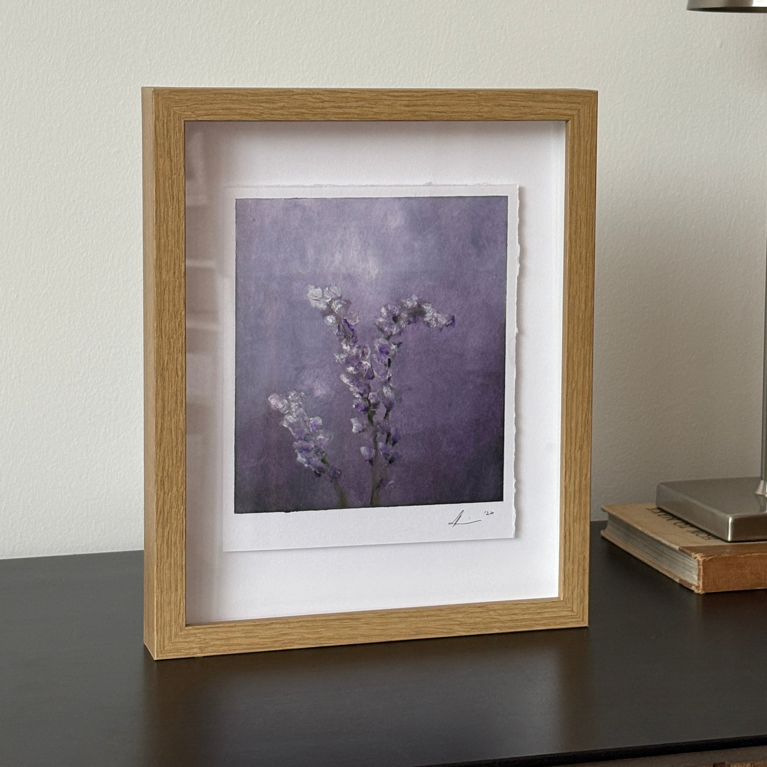 A square framed art print featuring a purple-toned floral branch illustration, beside a modern silver wall lamp.