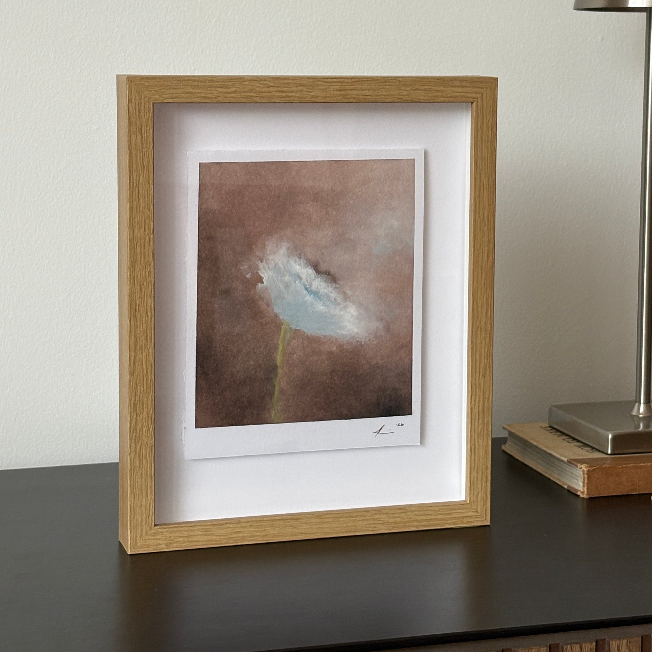 A framed abstract art print with a light oak wood frame and white mat